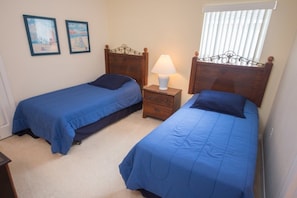 A bedroom with two single beds, a nightstand with a lamp, and a window with blinds.