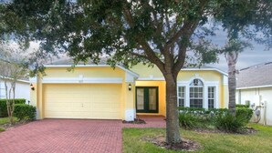 A yellow house with a garage, a brick driveway, and a tree in the front yard. - Ip60454 - Highgate at Legacy Park - 4 Bed 3 Baths Villa (Davenport)