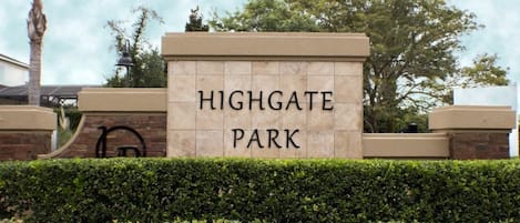 A sign for Highgate Park with a clear, legible font on a stone wall, surrounded by well-maintained hedges and trees.