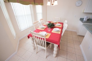 A dining area with a red tablecloth, white chairs, and a clock on the wall.