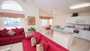 A modern living room with a red sofa and a kitchen area with white cabinets and a microwave. - Ip60454 - Highgate at Legacy Park - 4 Bed 3 Baths Villa (Davenport)