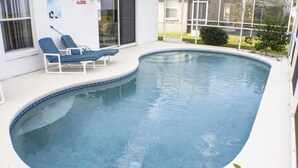 En pool med två solstolar och en glasdörr som leder till ett överbyggt område.
