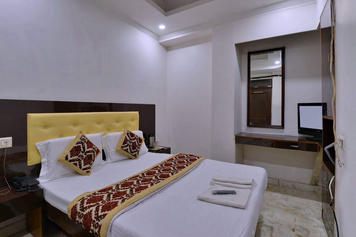 A hotel room with a bed, bedside table, and a mirror.