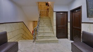 A marble staircase leading to a door marked 101, with a fire hose on the wall and two cushioned seating areas on either side. - PG International (New Delhi)