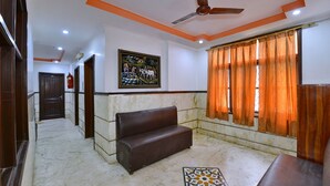 A hallway with a marble floor, a brown leather sofa, a ceiling fan, and a painting on the wall. - PG International (New Delhi)