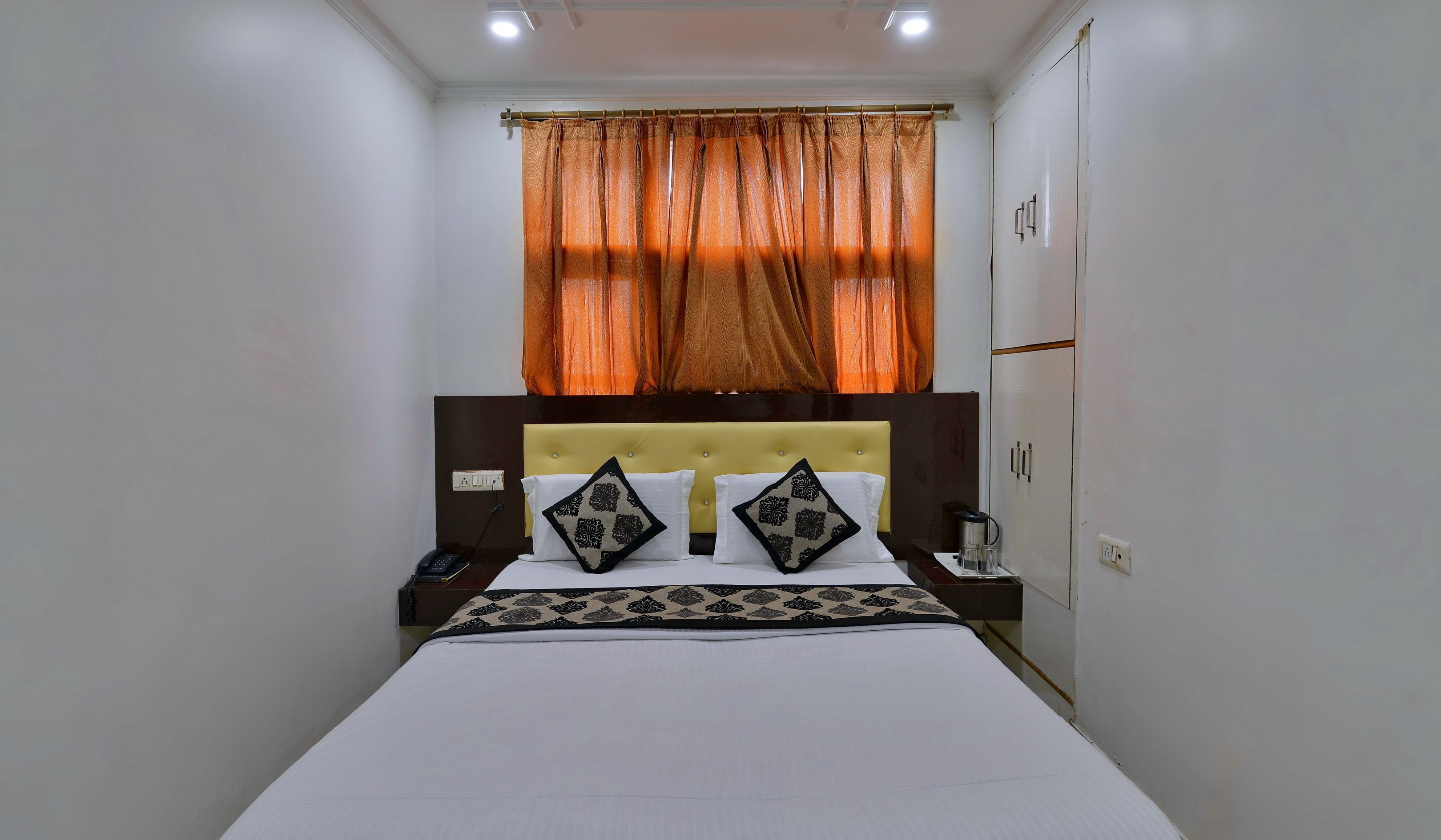 Quarto de hotel com uma cama, mesa de cabeceira, telefone, cafeteira e guarda-roupa.