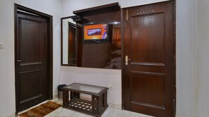 A hallway with two dark wooden doors, a small table with a glass top, and a television mounted on the wall. - PG International (New Delhi)