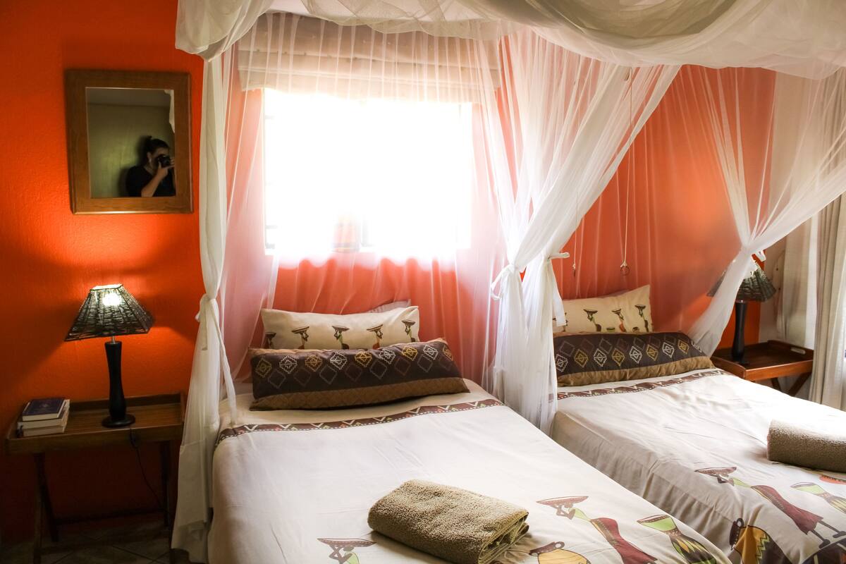 A room with two beds, each with a canopy, a bedside table with a lamp, and a mirror on the wall.