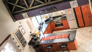 Uma cozinha com área de bar, um sofá com livros e um teto alto com vigas de madeira.