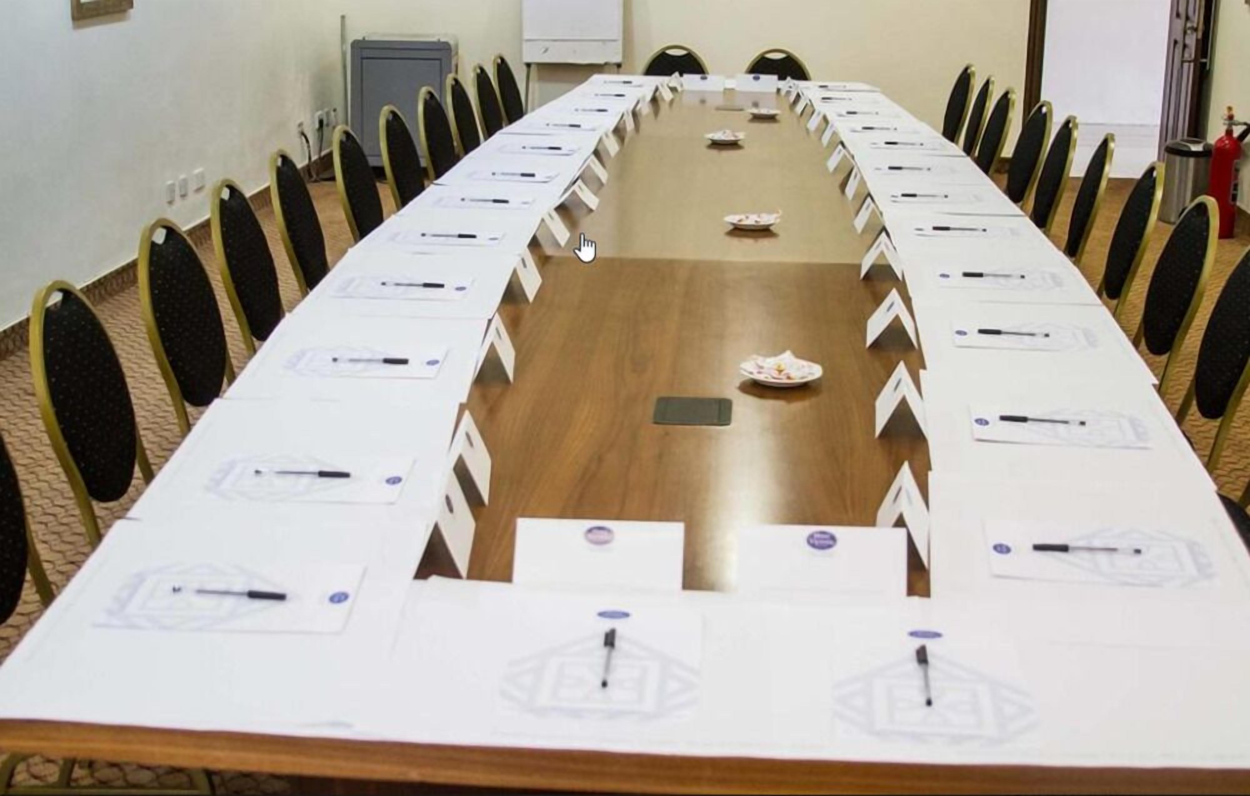 Un salón de conferencias con una larga mesa, sillas y placas con nombres.
