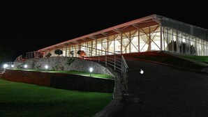 A modern building with a glass facade and a red roof, situated on a grassy slope with a paved pathway leading to it. - Hotel  Victoria (Blantyre)