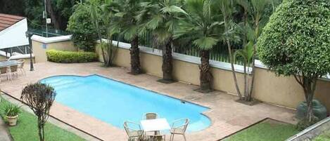 Una piscina rodeada de palmeras y un pequeño patio con mesa y sillas.