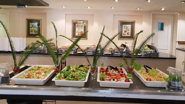 A buffet with various dishes, including salads and a pasta dish, in a well-lit room with framed artwork on the walls. - Hotel  Victoria (Blantyre)