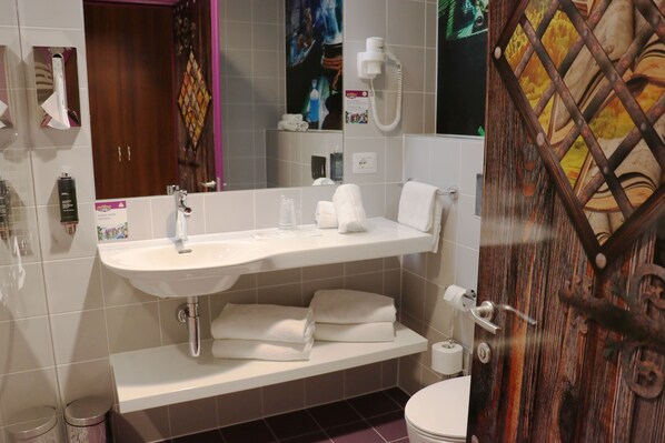 A bathroom with a white sink, mirror, and toilet. There are towels and toiletries on the sink. - Gardaland Magic Hotel (Castelnuovo del Garda)