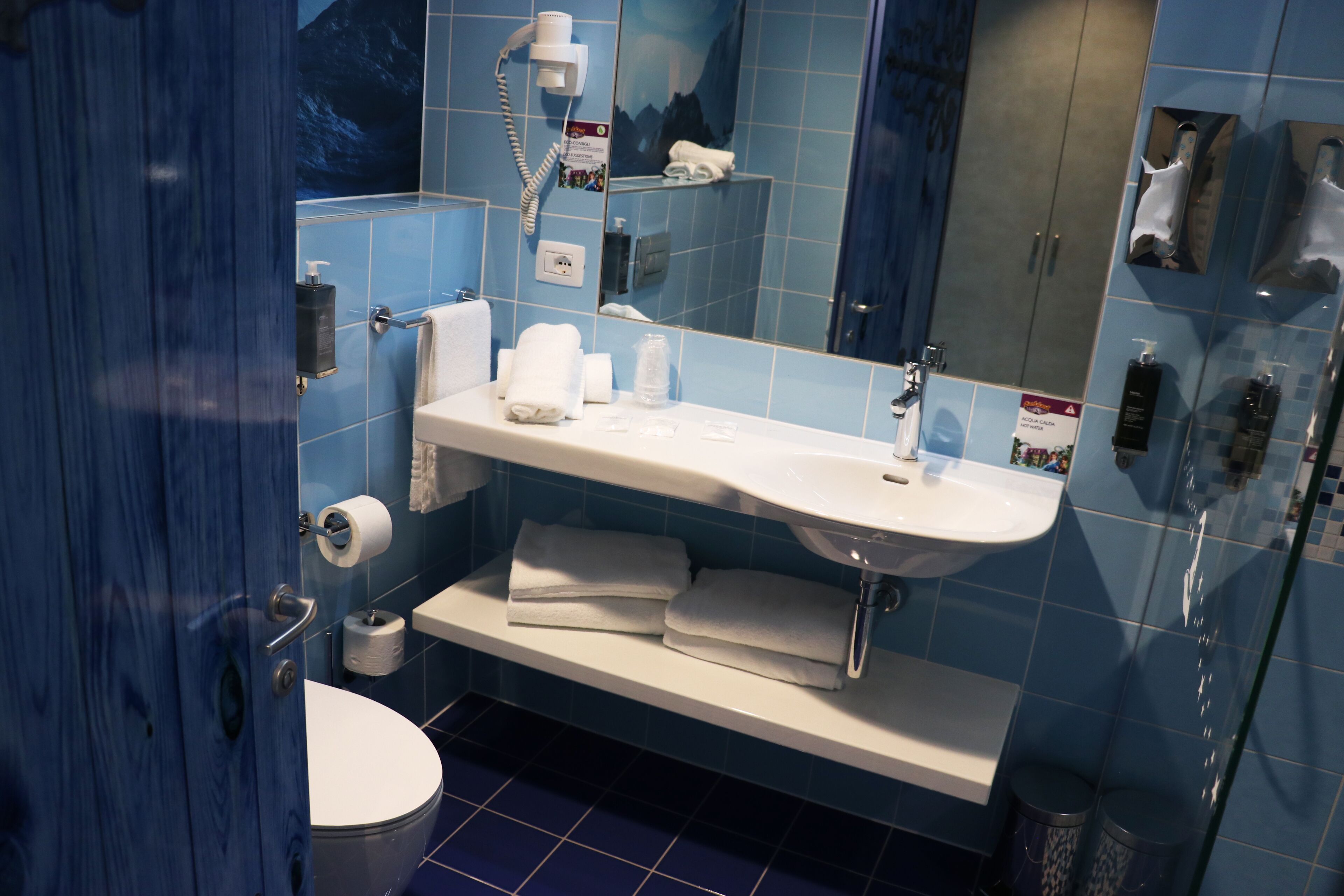 Un baño moderno con un lavamanos blanco, azulejos azules, una cabina de ducha de vidrio y un inodoro.