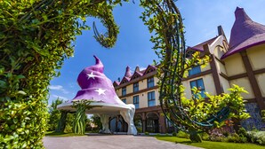 A fantasy-themed entrance with a large wizard hat structure, a castle-like building in the background, and a clear blue sky.