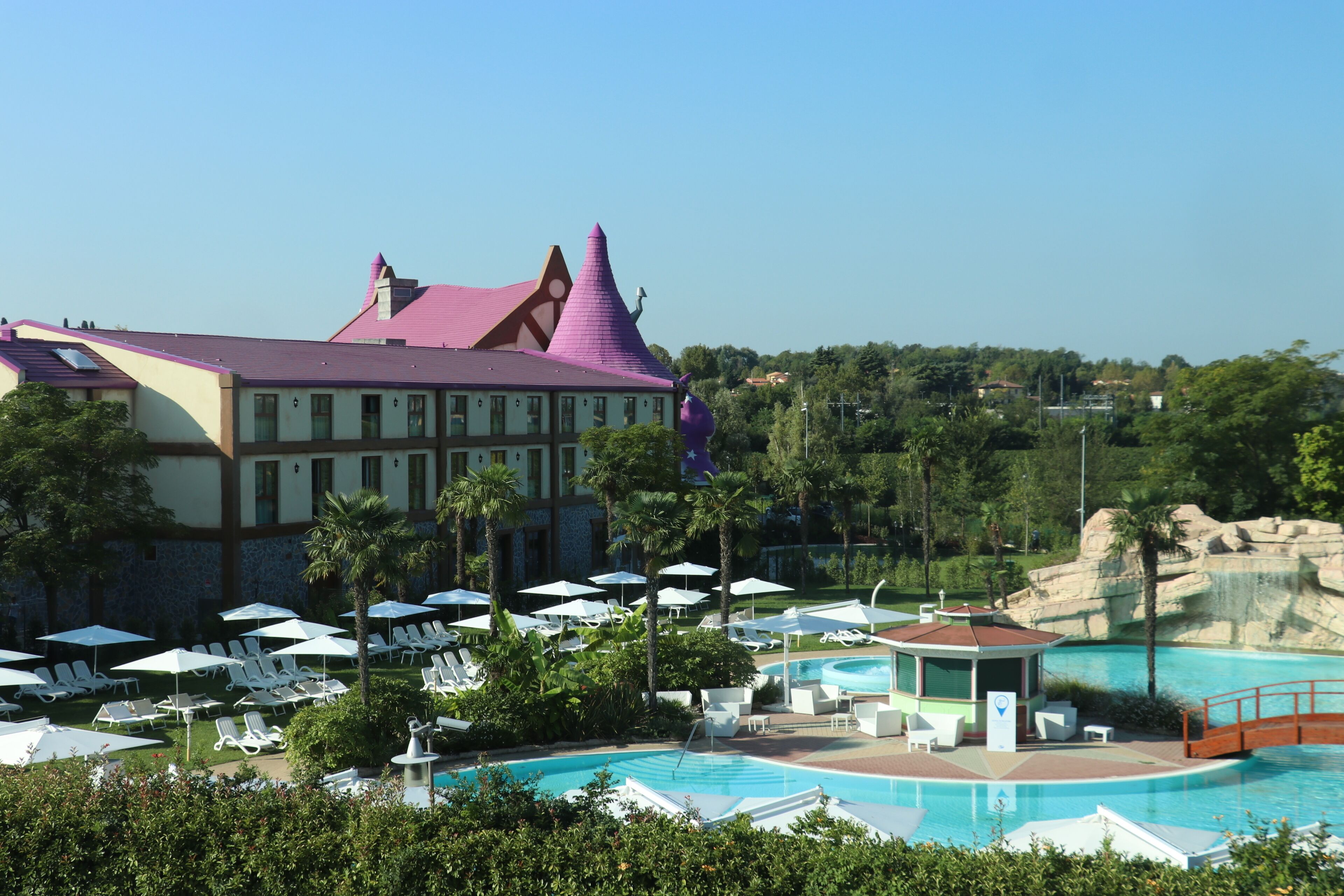 A resort with a swimming pool, lounge chairs, and a distinctive building with a purple roof.