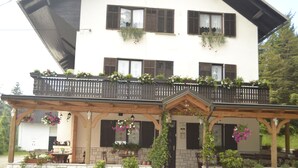 A two-story building with a balcony, potted plants, and hanging flower baskets. - Kmecki Hram (Idrija)