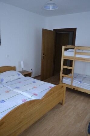 A room with a wooden bunk bed, a single bed with floral bedding, a bedside table with a lamp, and a door leading to another room. - Kmecki Hram (Idrija)