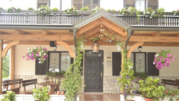 A covered outdoor seating area with a wooden pergola, potted plants, and a black door. - Kmecki Hram (Idrija)