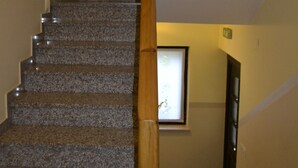 A staircase with granite steps and a wooden handrail, leading to a room with a window and a door. - Kmecki Hram (Idrija)
