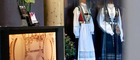 Ett receptionsområde med en träpelare, ett glasmontrinskåp med smycken och skyltdockor klädda i traditionella dräkter.