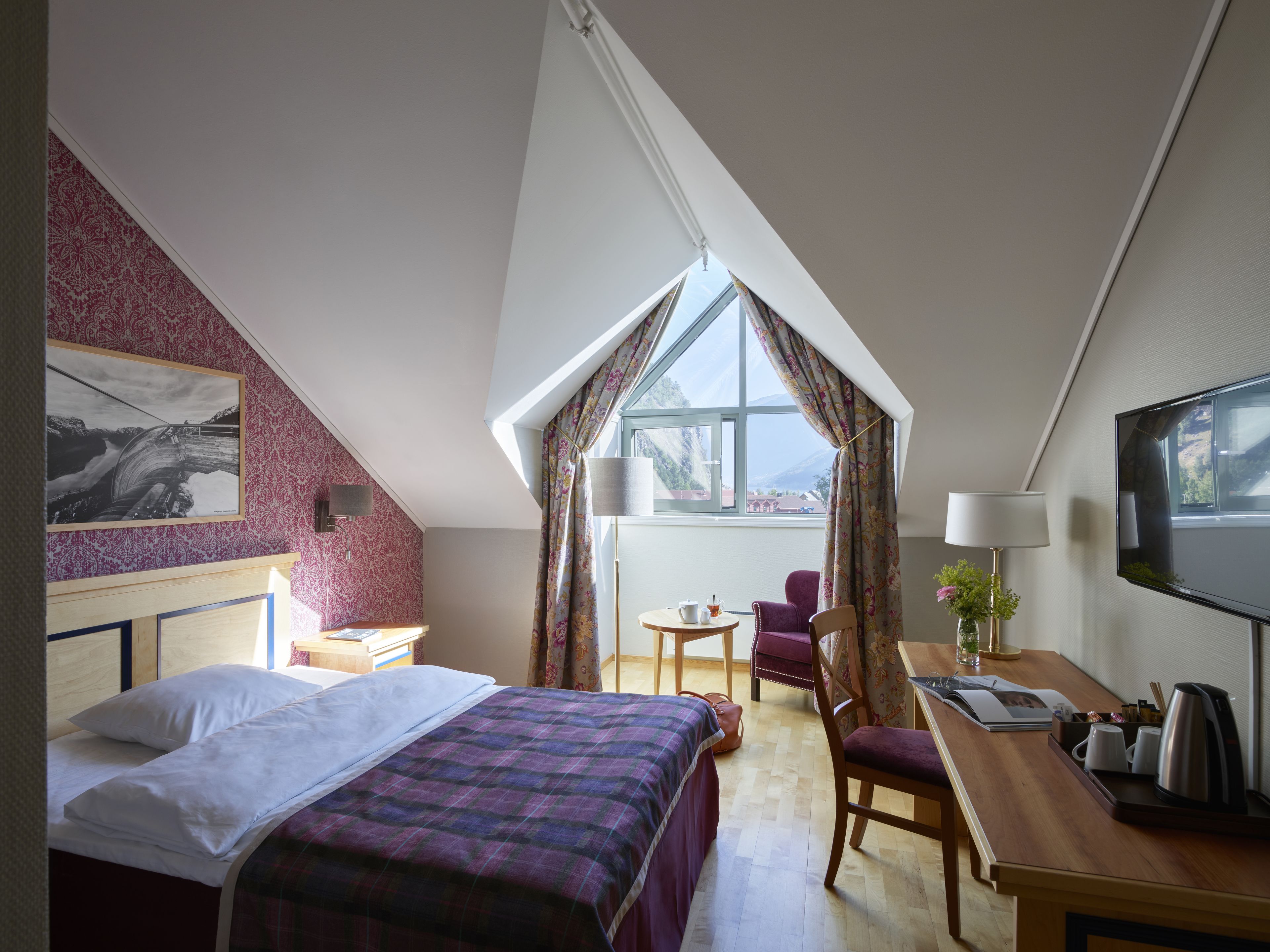 Une chambre d’hôtel avec un lit, un bureau, une chaise, une télévision et une fenêtre avec des rideaux.
