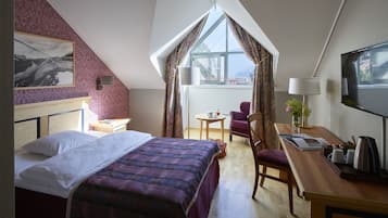 Une chambre d’hôtel avec un lit, un bureau, une chaise, une télévision et une fenêtre avec des rideaux.