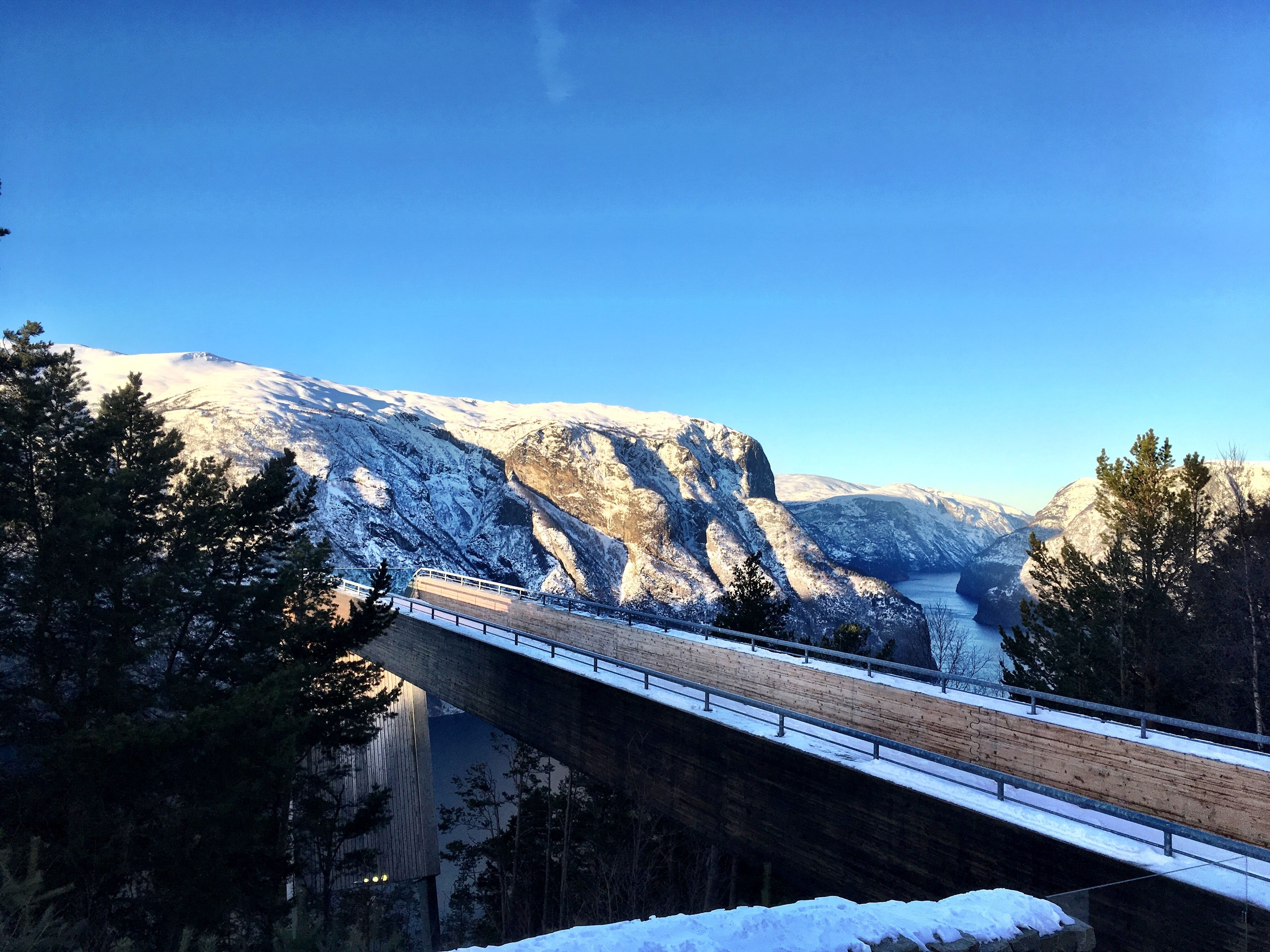 A snow-covered mountain landscape with a wooden bridge and a clear blue sky.
