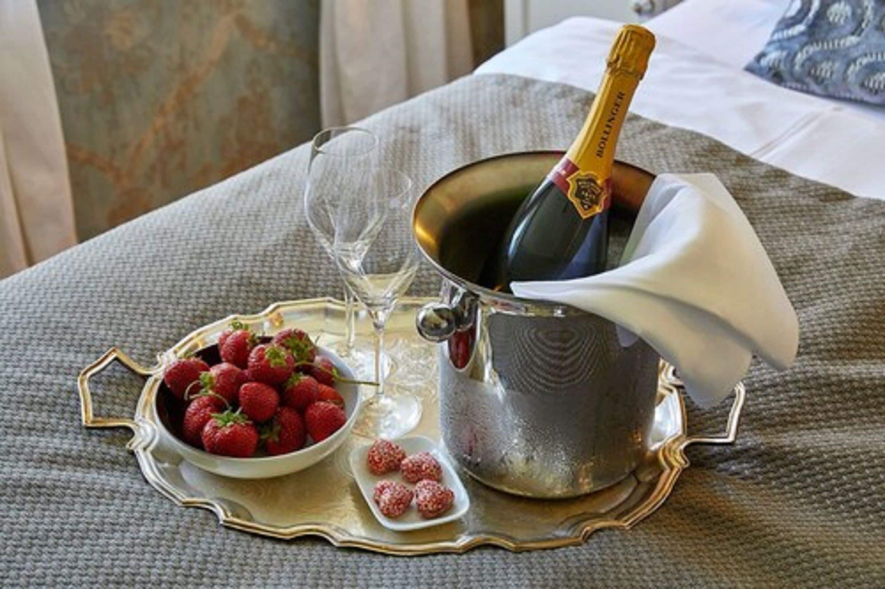 A champagne bottle in a silver bucket, a bowl of strawberries, and a wine glass on a tray.