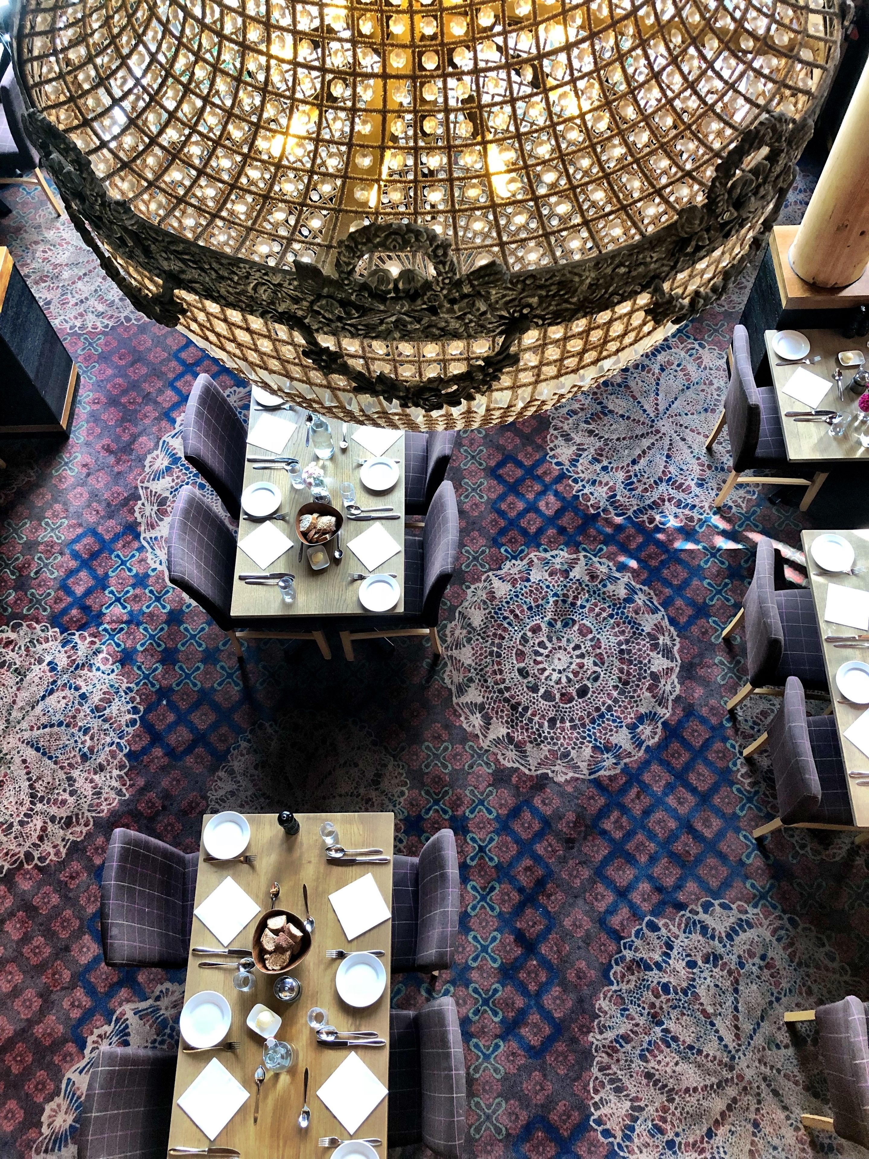 Un restaurante con varias mesas y sillas, una alfombra estampada y una lámpara decorativa en el techo.