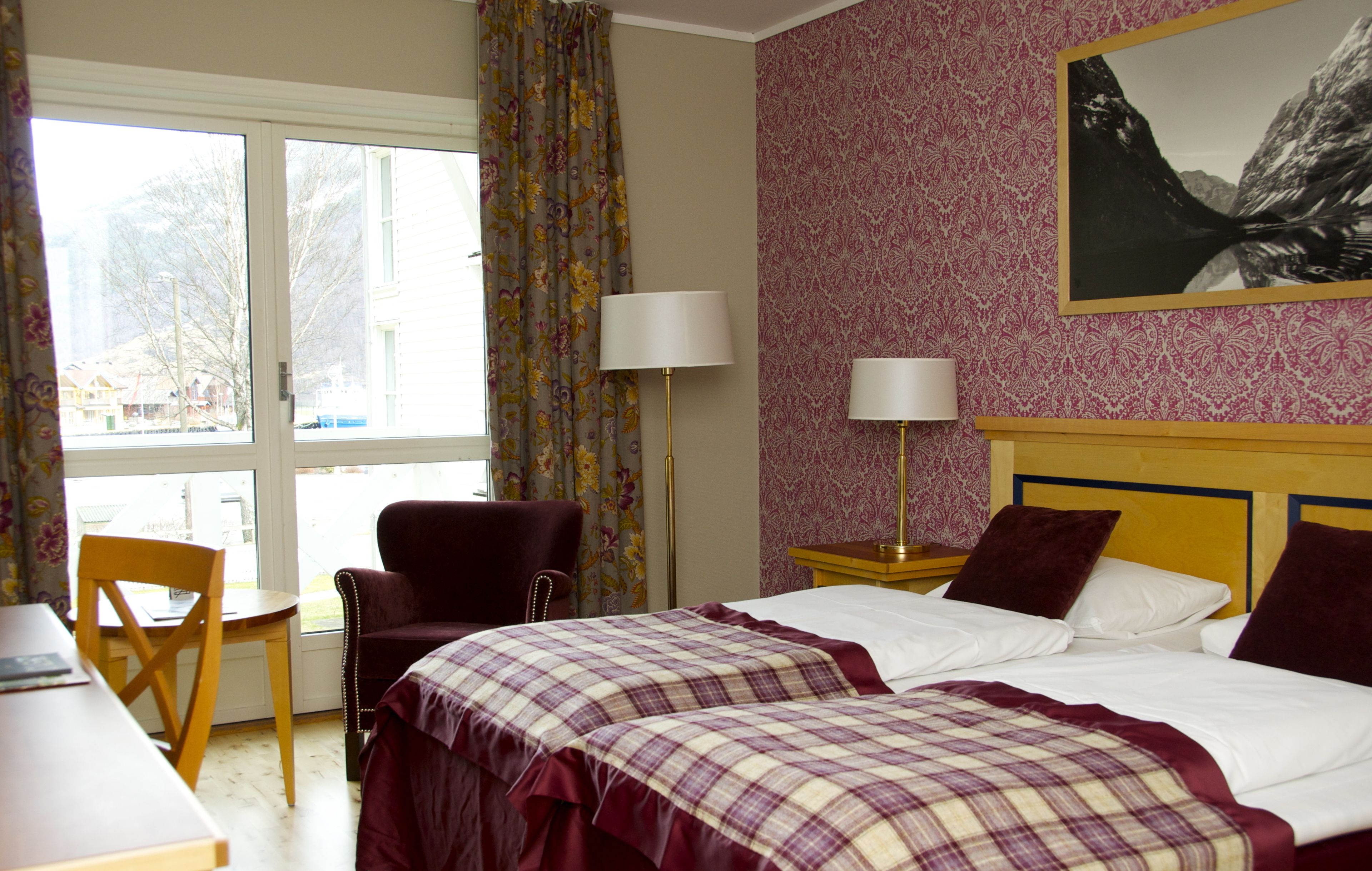 Ein Hotelzimmer mit Bett, zwei Nachttischlampen, einem Sessel, einem Tisch und einem Fenster mit Vorhängen.
