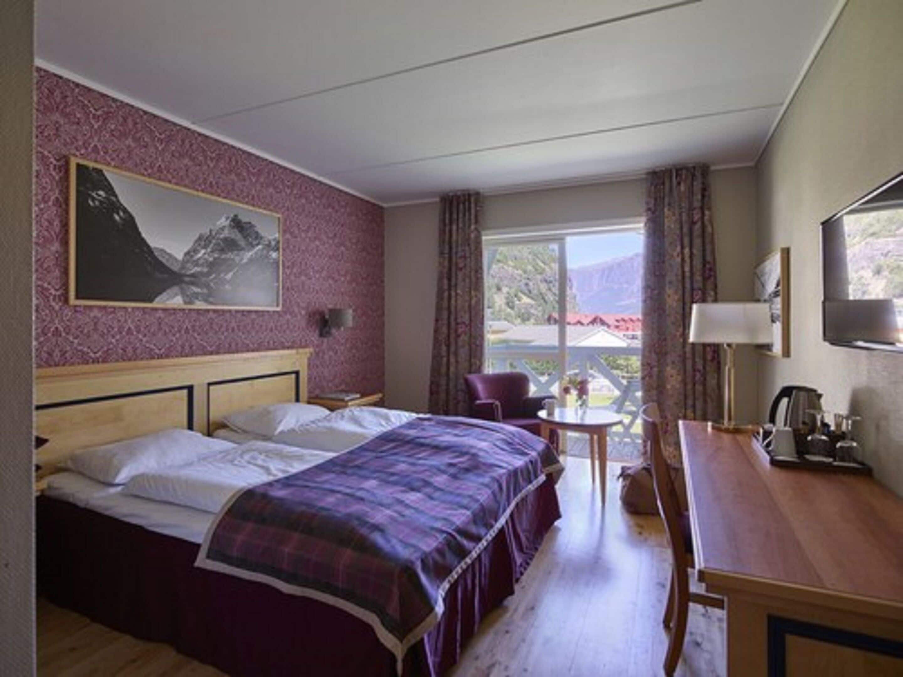 Habitación de hotel con cama, escritorio, silla, mesa y ventana con vista al exterior.