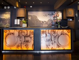 A reception desk with a large screen displaying a scenic landscape, wooden cabinets, and a clock on the wall.