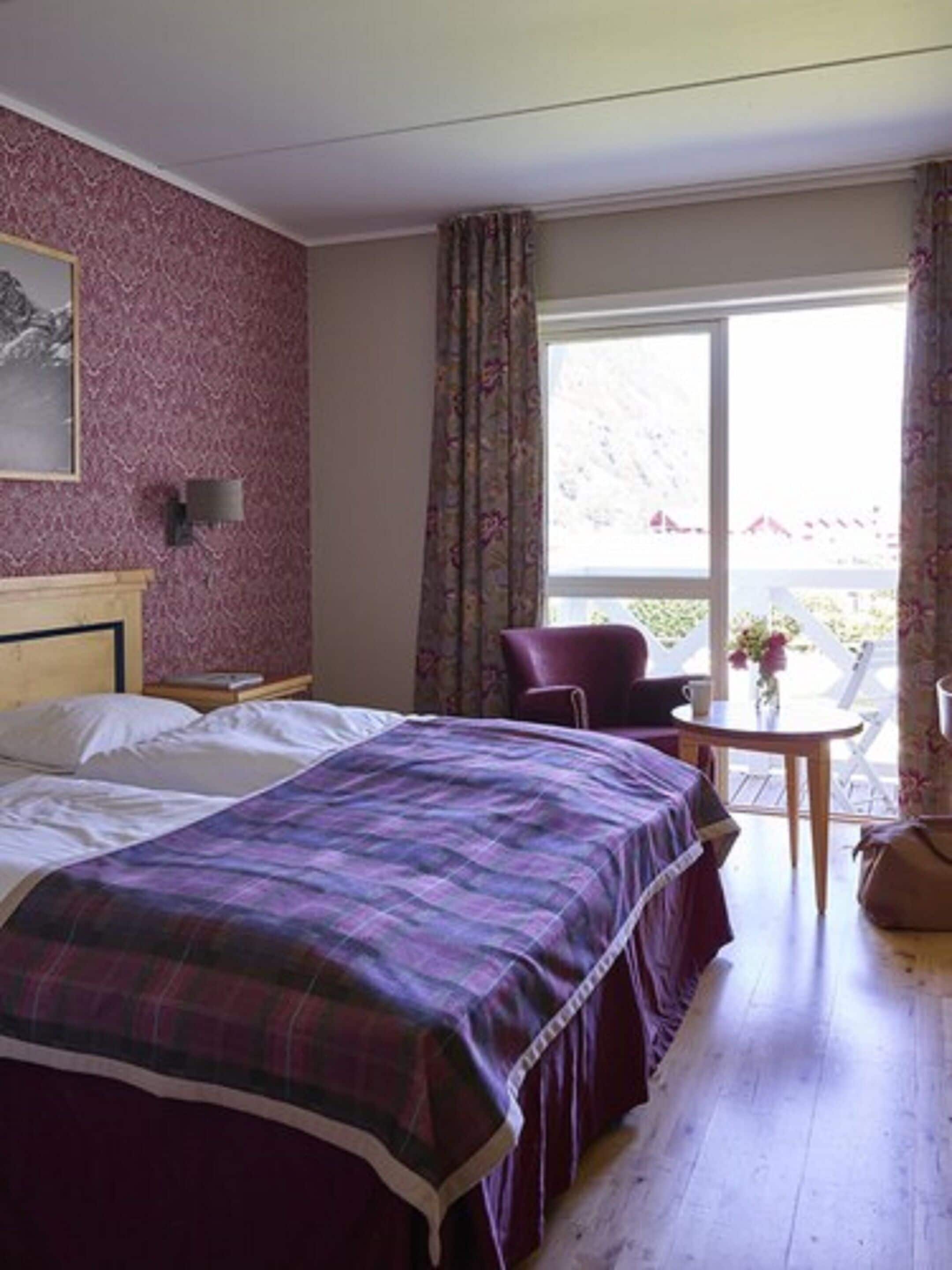 A hotel room with a bed, a chair, a table, and a window with curtains.