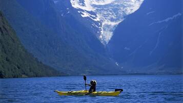 A kayaker in a yellow kayak on a calm body of water with mountains in the background.