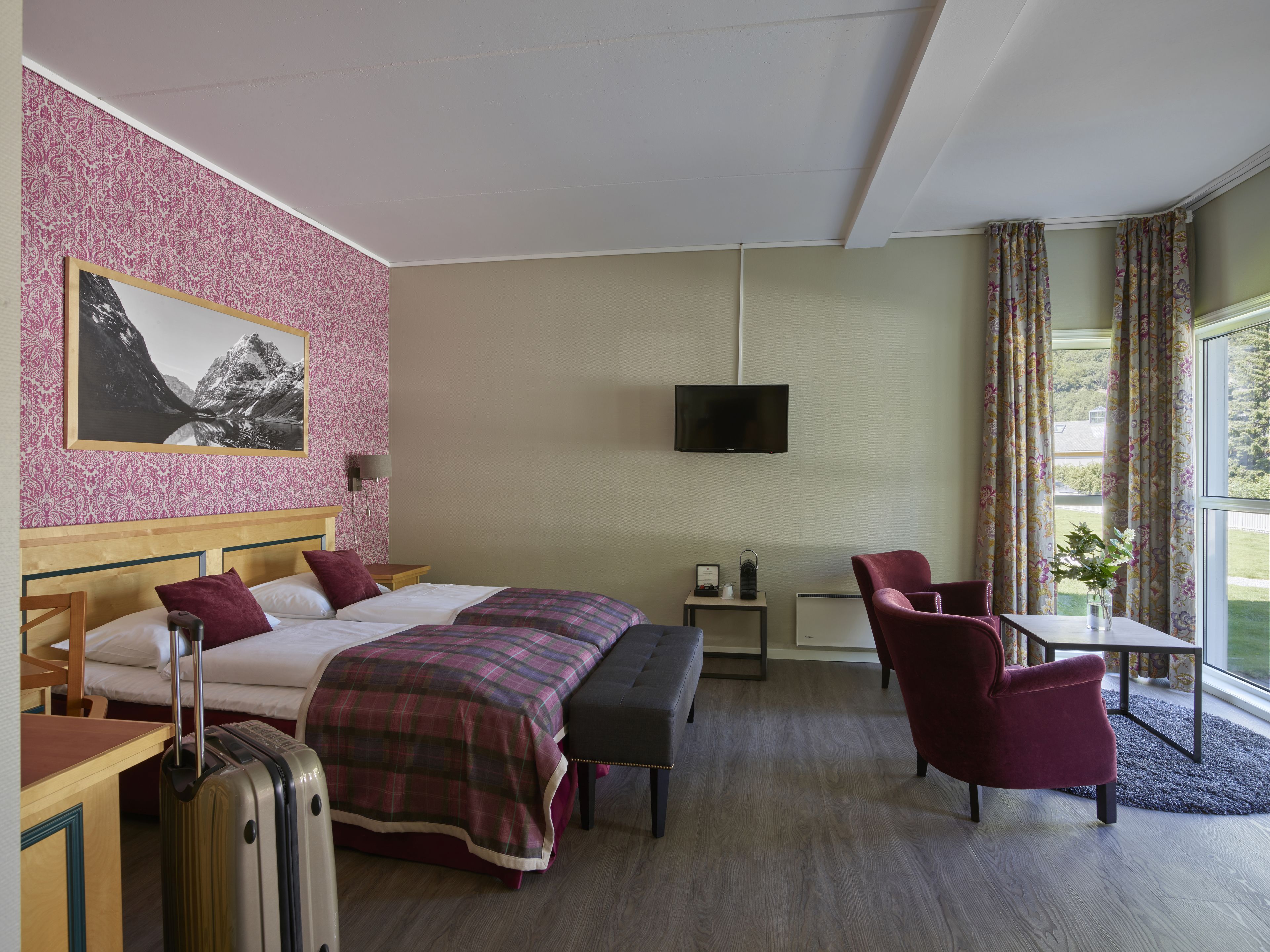 Hotellihuone, jossa on kaksi sänkyä, työpöytä, tuoli, televisio ja ikkuna, jossa on verhot.