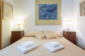 Habitación de hotel con una cama grande, dos mesitas de noche con lámparas, un cuadro en la pared y una ventana con persianas.