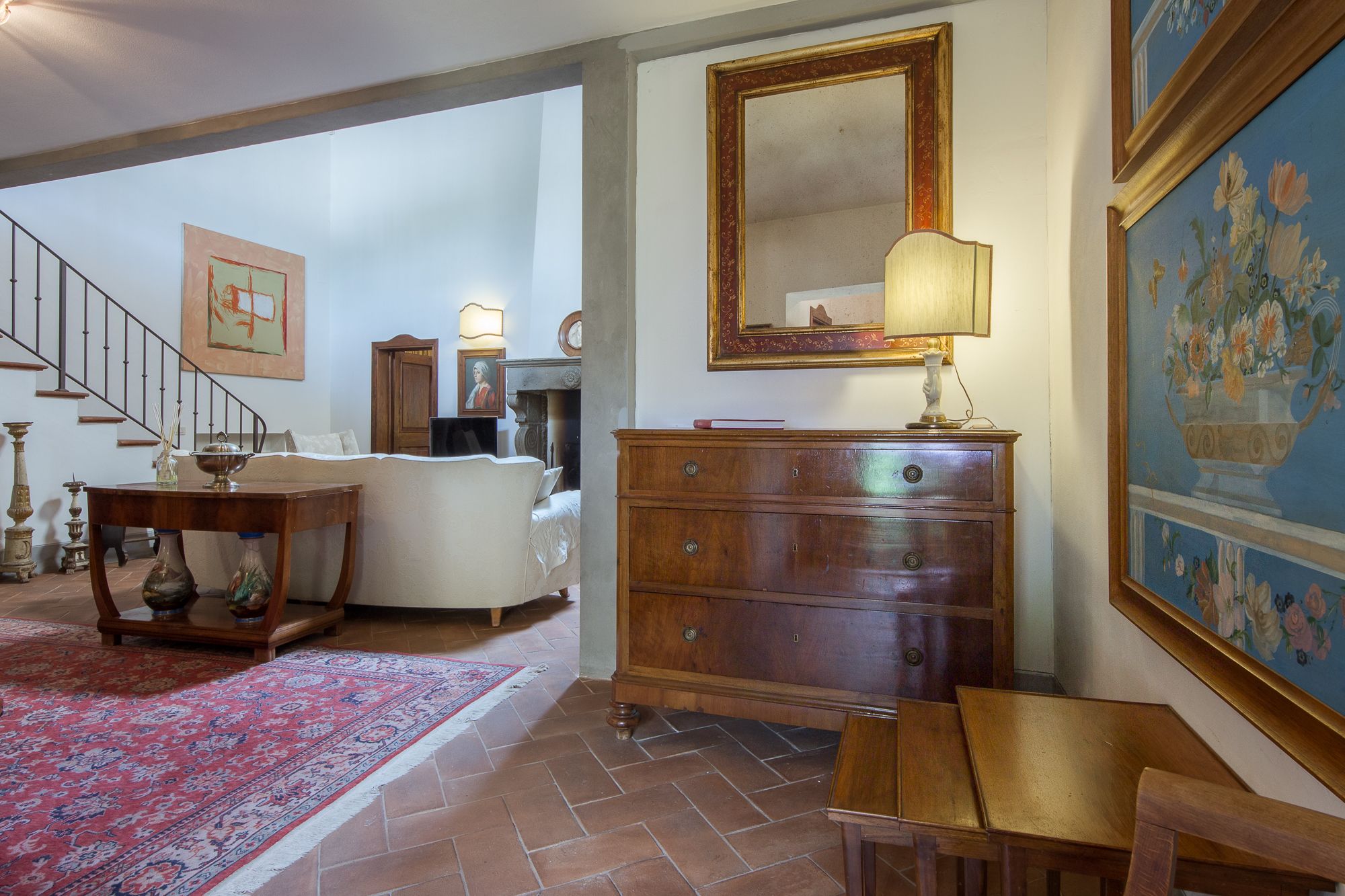 Een ruime woonkamer met een trap, een grote houten dressoir en een bloemistisch schilderij.