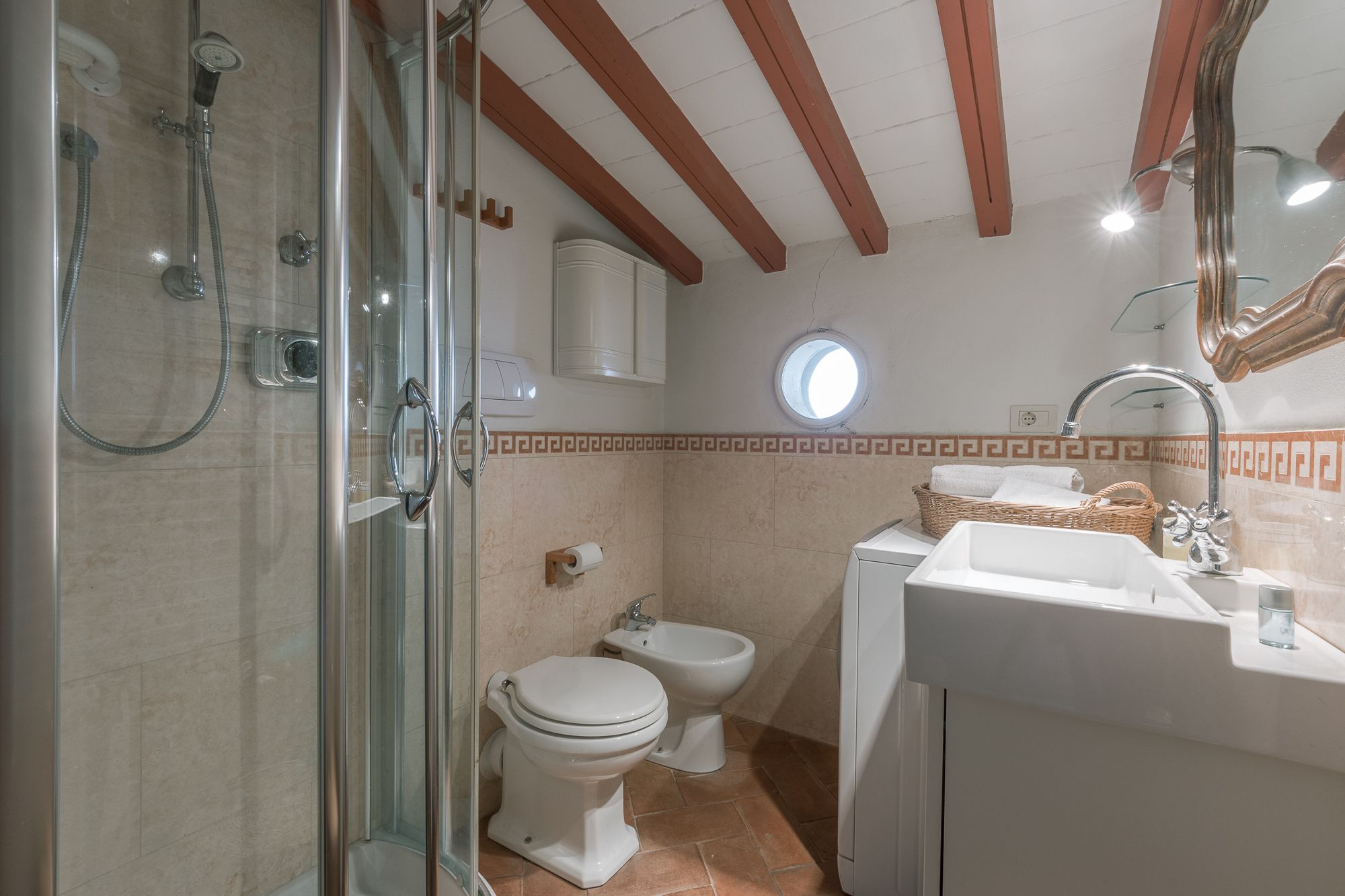 Un bany amb dutxa d'estuc de vidre, vàter, bidet, rentamig i mirall.
