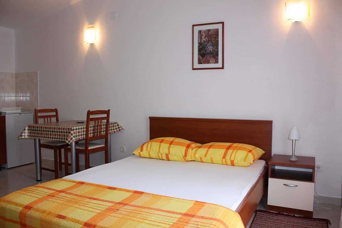 A bedroom with a bed, a nightstand, a table with chairs, and a wall-mounted picture.