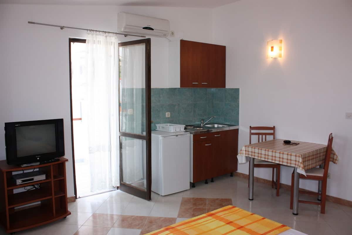 A compact kitchen with a refrigerator, stove, and wooden cabinets. There is a dining table with chairs and a television on a stand.