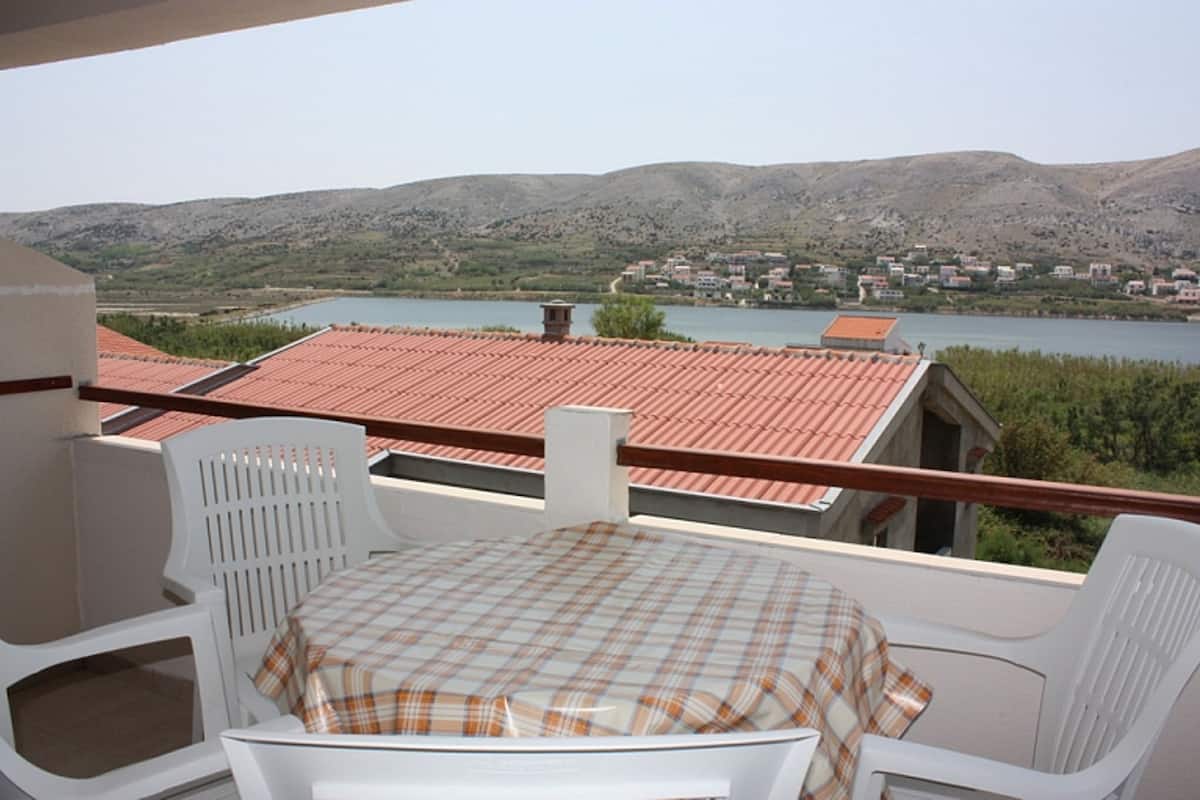 A terrace with a table and chairs, overlooking a lake and a town.