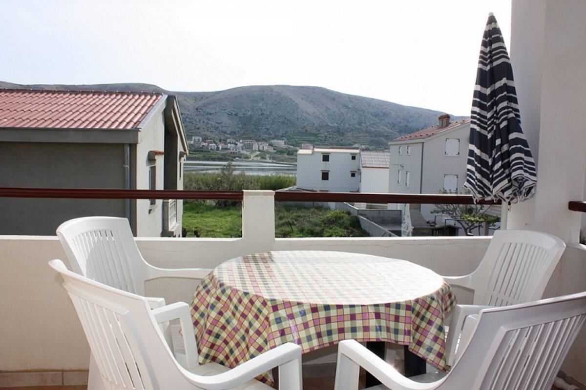 A balcony with a round table and white chairs, overlooking a mountainous landscape and buildings.