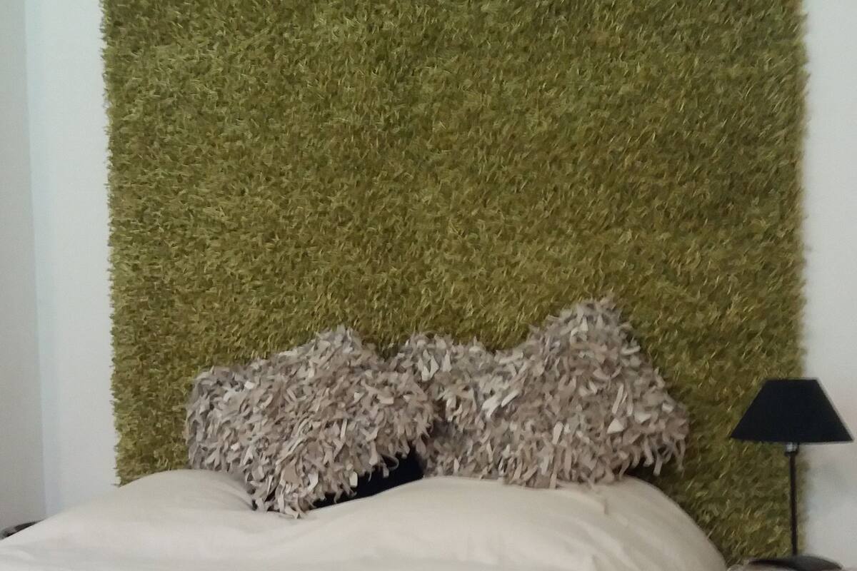 A bed with a green textured headboard, a white and brown bedspread, and a red pillow. A floor lamp is visible to the right.