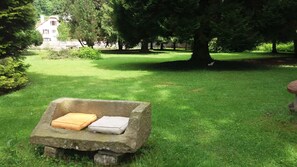 A stone bench with cushions in a grassy park area. - Au Pied des milles Étangs- LES CAPUCINS (Faucogney-et-la-Mer)