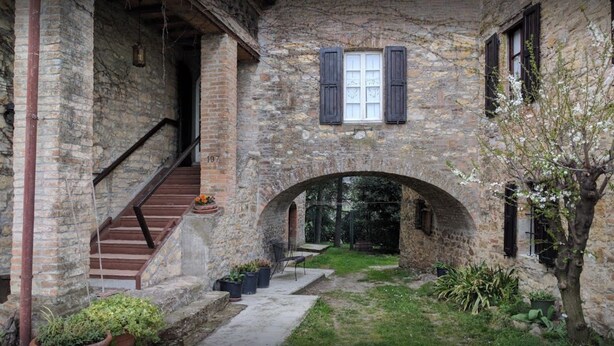 Un edificio de piedra con una escalera que conduce a un segundo piso, un arco y plantas en macetas.