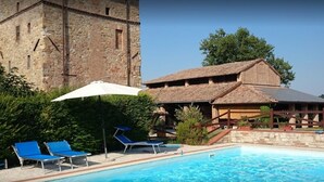 Un edificio de piedra con zona de piscina, que incluye sillas de descanso y una estructura con techo de paja.