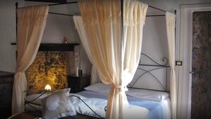 Una cama con dosel frente a una pared de piedra, con una vela encendida.