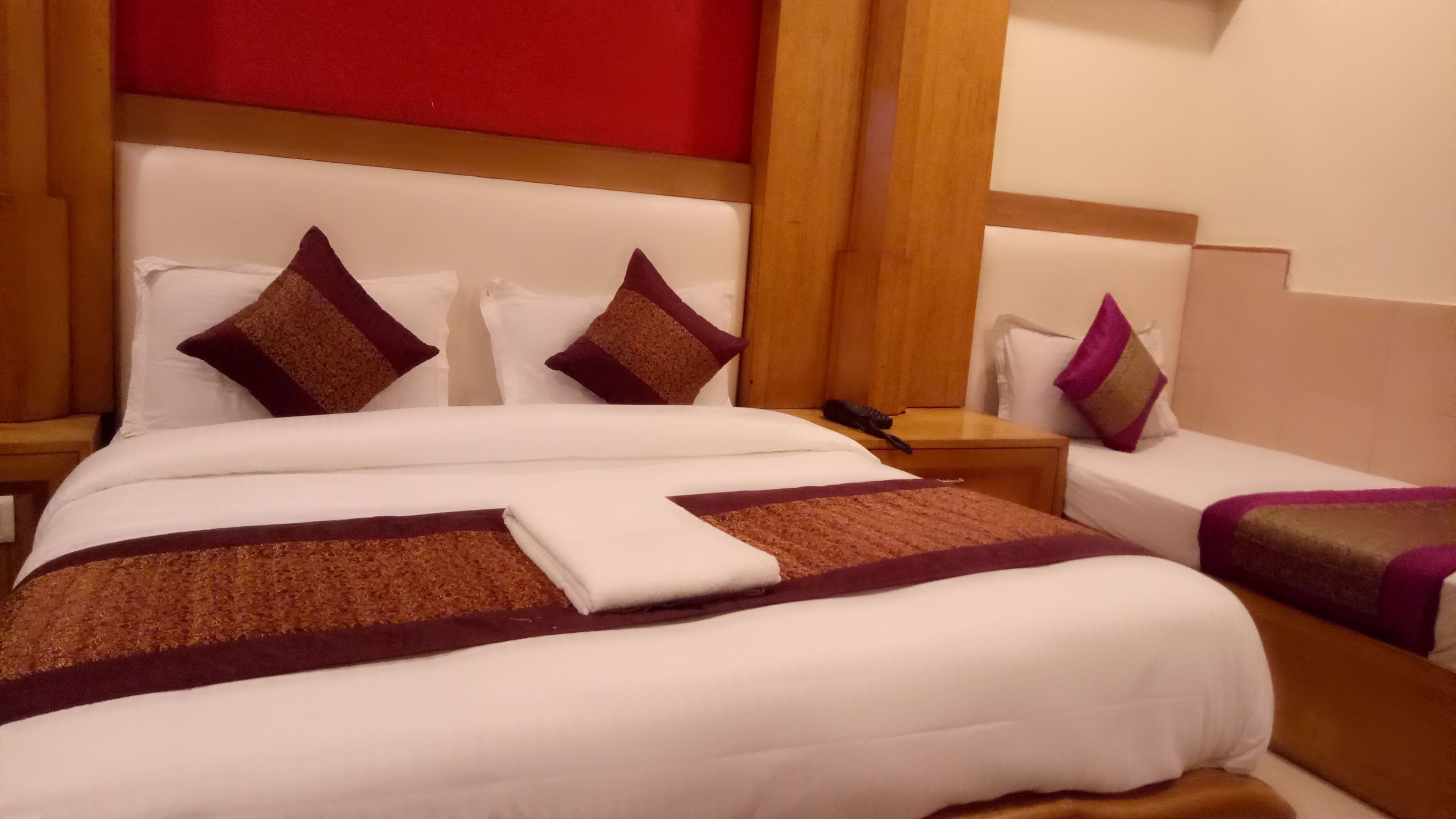 A hotel room with a large bed, two smaller beds, wooden headboards, and a red accent wall.